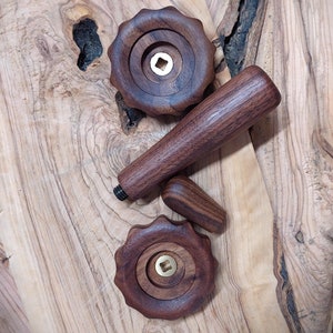 May include: Three wooden knobs with brass inserts. The knobs are dark brown and have a smooth, polished finish. The knobs are arranged on a light brown wooden surface.