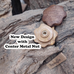 Peut inclure: Deux boutons en bois avec un motif en étoile. Le plus grand bouton a un écrou métallique au centre. Le plus petit bouton est brun et le plus grand bouton est brun clair. Les boutons sont sur un morceau de bois.