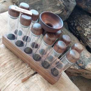 May include: A wooden spice rack with glass vials and wooden lids. The rack holds several clear glass tubes with dark wooden caps, and a small wooden bowl. The text "Nepacoffee" is on a small wooden sign.