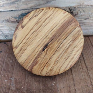 Puede incluir: Una tabla de cortar redonda de madera con un patrón de veta de madera natural. La tabla está hecha de madera marrón claro con vetas marrón oscuro.