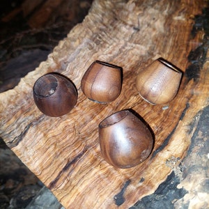 May include: Four wooden beads in a natural brown color, with a smooth, rounded shape. The beads are arranged on a piece of wood with a brown and black grain pattern.