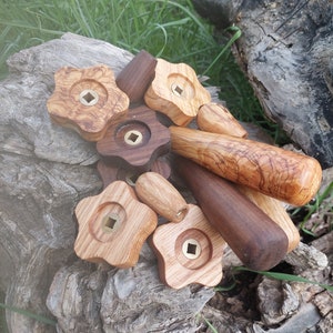 May include: A collection of wooden knobs with brass inserts, some shaped like stars, others round, and a few long and cylindrical. The knobs are arranged on a piece of weathered wood.