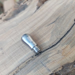 Könnte beinhalten: Ein silberner Metallknopf mit abgerundeter Oberseite und einem Gewinde am Boden.