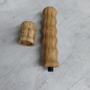 Puede incluir: Juego de mango y tapa de madera de dos piezas. El mango es de color marrón claro con un diseño acanalado. La tapa es una pieza más pequeña y a juego. Ambas piezas tienen un veteado natural y una base roscada.