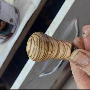 May include: A wooden knob with a brown and light brown wood grain pattern. The knob has a metal screw on the bottom.