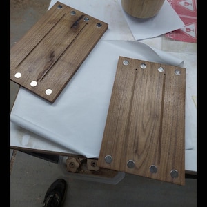 May include: Wooden cutting boards with three grooves and embedded magnets. The boards are rectangular and made of a dark wood. A wooden cup is also visible in the image.
