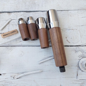 Puede incluir: Cuatro herramientas de tamper de madera y cromo para máquinas de espresso, dispuestas en orden de tamaño de la más pequeña a la más grande. El tamper más grande tiene un extremo roscado.