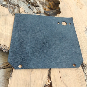 May include: A black leather patch with two round holes and a larger oval hole. The patch has a textured surface.