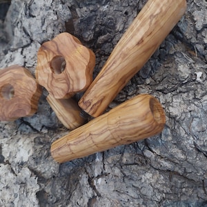 Puede incluir: Cuatro tapones de botella de madera de olivo, dos son redondos con un agujero en el centro, uno tiene forma de estrella con un agujero en el centro y uno es un cilindro largo.
