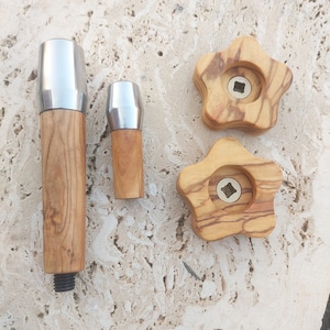May include: Three wooden knobs with a star shape and a metal insert in the center. The knobs are made of olive wood and have a natural wood finish. The knobs are different sizes.