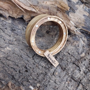 May include: A wooden coffee cup holder with a circular design and embedded magnets. A small wooden tag with the text "Nepacoffee" is attached. The holder is made of light-colored wood and sits on a textured wooden surface.