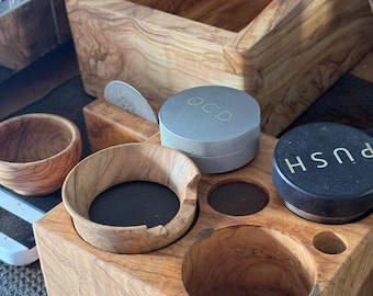 Puede incluir: Una estación de café de madera con un contenedor de metal gris etiquetado como "OCD", un contenedor negro etiquetado como "PUSH" y un tazón de madera. La estación tiene múltiples compartimentos para guardar accesorios de café.