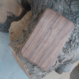 Könnte beinhalten: Ein rechteckiges Holztablett aus dunklem Walnussholz. Das Tablett hat eine glatte, polierte Oberfläche und abgerundete Kanten.