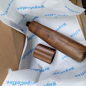 May include: A cylindrical dark brown wooden handle with a threaded metal screw at one end and a separate matching wooden cap piece. The items are resting on white tissue paper printed with the repeating blue text NepoCoffee.