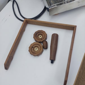 Puede incluir: Componentes de máquina de espresso de madera, incluyendo dos perillas redondas con detalles de latón, un mango cilíndrico y un marco rectangular. Las piezas están dispuestas sobre una superficie blanca, posiblemente para un proyecto de bricolaje o reparación.