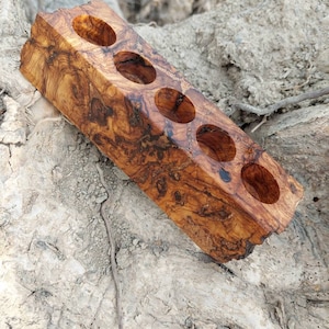 May include: A wooden holder with six round holes, made from olive wood with a natural brown and black wood grain pattern.