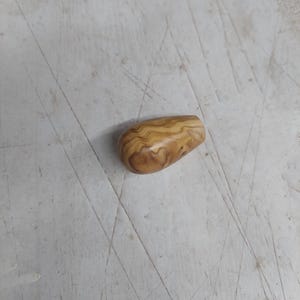 Könnte beinhalten: Ein kleines, glattes Holzobjekt mit abgerundeter Form und hellbrauner Farbe. Die Holzmaserung weist ein einzigartiges Muster aus dunkleren braunen Wirbeln und Linien auf. Das Objekt scheint ein Griff oder ein dekoratives Stück zu sein.