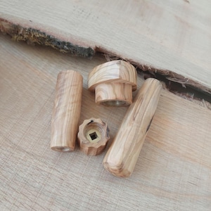 May include: A collection of wooden furniture hardware components, including knobs and cylindrical handles. The pieces are made of light-colored wood with visible grain and are arranged on a wooden surface.