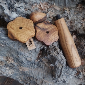 Op de afbeelding: Drie houten stukken voor een houten puzzel, twee zijn stervormig met een gat in het midden, één is rond, alle zijn gemaakt van olijfhout met een natuurlijke houtnerf.