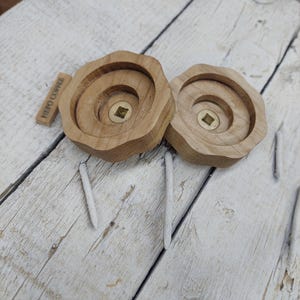 May include: Two wooden knobs with a square brass insert in the center. The knobs are unfinished and have a natural wood color. The text "PUERTO COPELE" is engraved on one of the knobs.