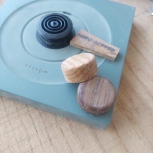 Pode incluir: Uma chaleira elétrica Fellow Stagg EKG verde com uma base preta e uma pega de madeira. A chaleira está sobre uma superfície de madeira. O texto "NEPO COFFEE" é visível numa etiqueta de madeira.