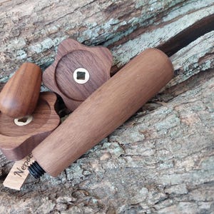May include: A set of wooden bottle stoppers, featuring a star-shaped design and a cylindrical handle. The set includes a stopper, two star-shaped pieces, and a cylindrical piece. The wood is a warm brown colour, and the set is on a textured wooden surface.
