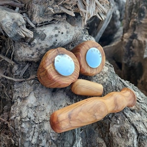 Può includere: Una collezione di strumenti per massaggio in legno fatti a mano. Due pezzi arrotondati con centri a specchio e la parola "VAGHE" sono esposti con altri due pezzi di legno, tutti con finitura a venatura naturale.