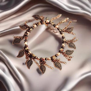 May include: A gold-toned bracelet with a delicate chain and dangling leaf charms. The bracelet is made of metal and has a beaded design.