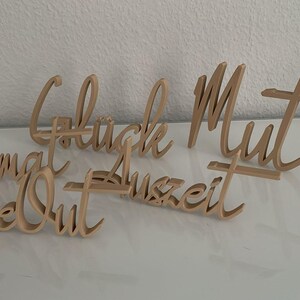 May include: Five wooden signs with different words written on them. The words are "Heimat", "Time Out", "Gl&uuml;ck", "Mut", and "Auszeit".