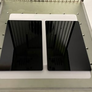 May include: Two black rectangular panels are placed on a white surface with a gray background. The panels are positioned side-by-side.