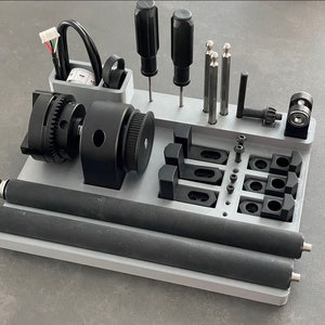May include: A gray 3D printed organizer with various tools and accessories. It includes a black gear-driven motor, two black rollers, a black and silver drill bit, and several black clamps.