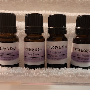 May include: Four small brown glass bottles with black caps, each containing essential oil. The labels are white with purple text and list the scents: Orange (Sweet), Tea Tree, Eucalyptus, and Patchouli (Dark).