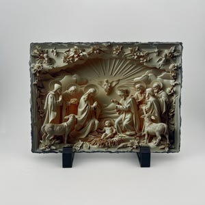 May include: A white stone relief sculpture depicting the Nativity scene. The sculpture features the baby Jesus, Mary, Joseph, and other figures, including angels and animals. The sculpture is set against a background of clouds and stars.