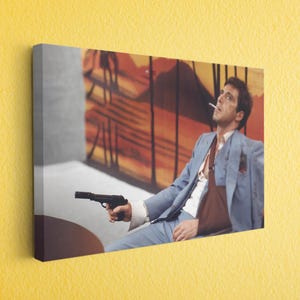 May include: Canvas print featuring a man in a light blue suit, holding a black handgun. He is smoking a cigarette. The background has orange and brown tones.