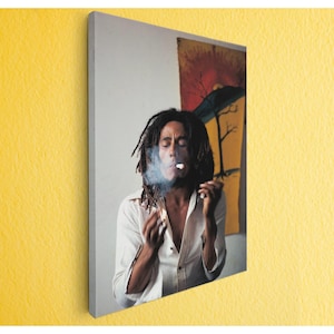 May include: A canvas print featuring a portrait of a person with dreadlocks smoking. The person is wearing a white shirt, and smoke is visible. A colorful painting hangs in the background.