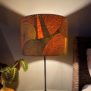 May include: A black table lamp with a geometric patterned lampshade in shades of orange, yellow, and black. The lamp is on a glass table top.