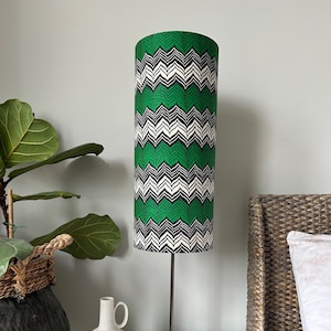 May include: A black and green patterned lampshade with a black metal base. The lamp is on a glass table top with two white ceramic vases.