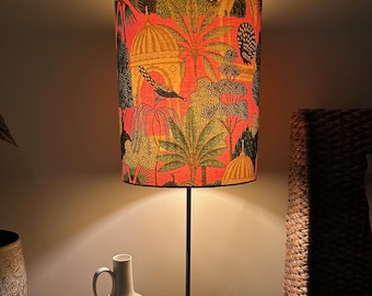 Könnte beinhalten: Eine Tischlampe mit einem rosa-grünen Lampenschirm mit Vogel- und Palmenmotiven. Die Lampe steht auf einem Glastisch mit einer weißen Vase.