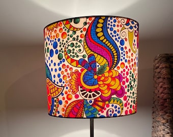 May include: A black table lamp with a colourful patterned lampshade. The lampshade features a white background with a variety of colourful swirls, dots, and abstract shapes in shades of red, orange, yellow, green, blue, and purple.
