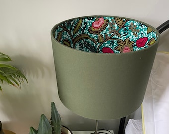 May include: A green lampshade with a floral pattern lining the inside. The lampshade is on a table next to a potted cactus.
