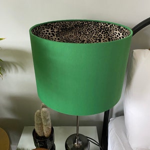Op de afbeelding: Een groene lampenkap met een luipaardprint voering. De lampenkap staat op een tafel met een zilveren lampvoet.