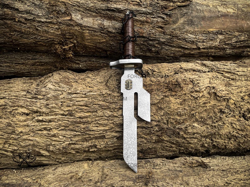 May include: A metal dagger featuring a textured silver blade with a distinct cutout notch and a small rectangular emblem. The handle is wrapped in dark brown leather with a black cord lacing detail and a silver crossguard separating the blade.