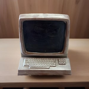 May include: A silver-coloured computer figurine with a black screen and a keyboard. The figurine is made of a smooth, shiny material.