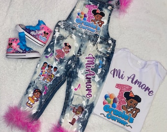 May include: A denim overall set with a matching white onesie and sneakers. The overalls and sneakers have pink feather trim and feature graphics with the text "Mi Amore" and "Gracie's Corner". The onesie also has the text "Mi Amore".