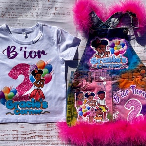 May include: A white t-shirt and denim overall set. The t-shirt features the text "B'ior" and "Gracie's Corner" with a number 2 and a cartoon girl with balloons. The denim overall has a pink feather trim.