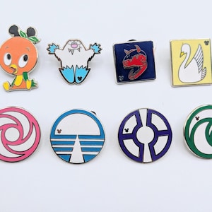 May include: A collection of eight enamel pins with various designs. The pins include an orange bird, a white yeti, a red dinosaur, a white swan, and several circular designs with geometric patterns and Mickey Mouse icons.