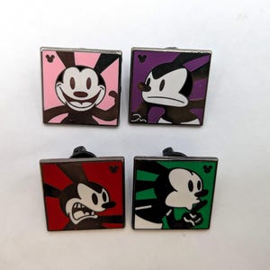 May include: Four square enamel pins featuring the cartoon character Oswald the Lucky Rabbit. Each pin has a different expression and background color: pink, purple, red, and green. The pins have a silver border and a black pin back.