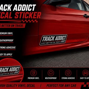 Op de afbeelding: Een rechthoekige vinyl sticker met de witte tekst TRACK ADDICT en de zin LIFE'S BETTER ON TRACK met een geblokte vlag-afbeelding. De sticker is zwart met een witte rand en is aangebracht op de zijkant van een rode auto.