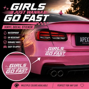 Op de afbeelding: Een witte vinyl sticker met de tekst GIRLS JUST WANNA GO FAST, kleine sterretjes en een geblokt vlagpatroon. De sticker is aangebracht op de achterbumper van een roze auto, met een cirkelvormige inzet die het ontwerp van de sticker uitvergroot.