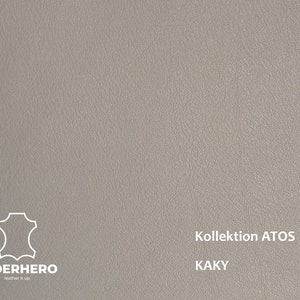 May include: A close-up of a textured, light grey leather sample. The sample is labelled "Kollektion ATOS KAKY" and features the Lederhero logo.